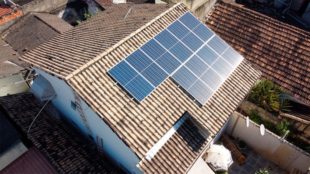 Vista aérea feita por drone da instalação de energia solar residencial em telhado cerâmico, refletindo a luz do sol, localizado em São Gonçalo, no Rio de Janeiro.